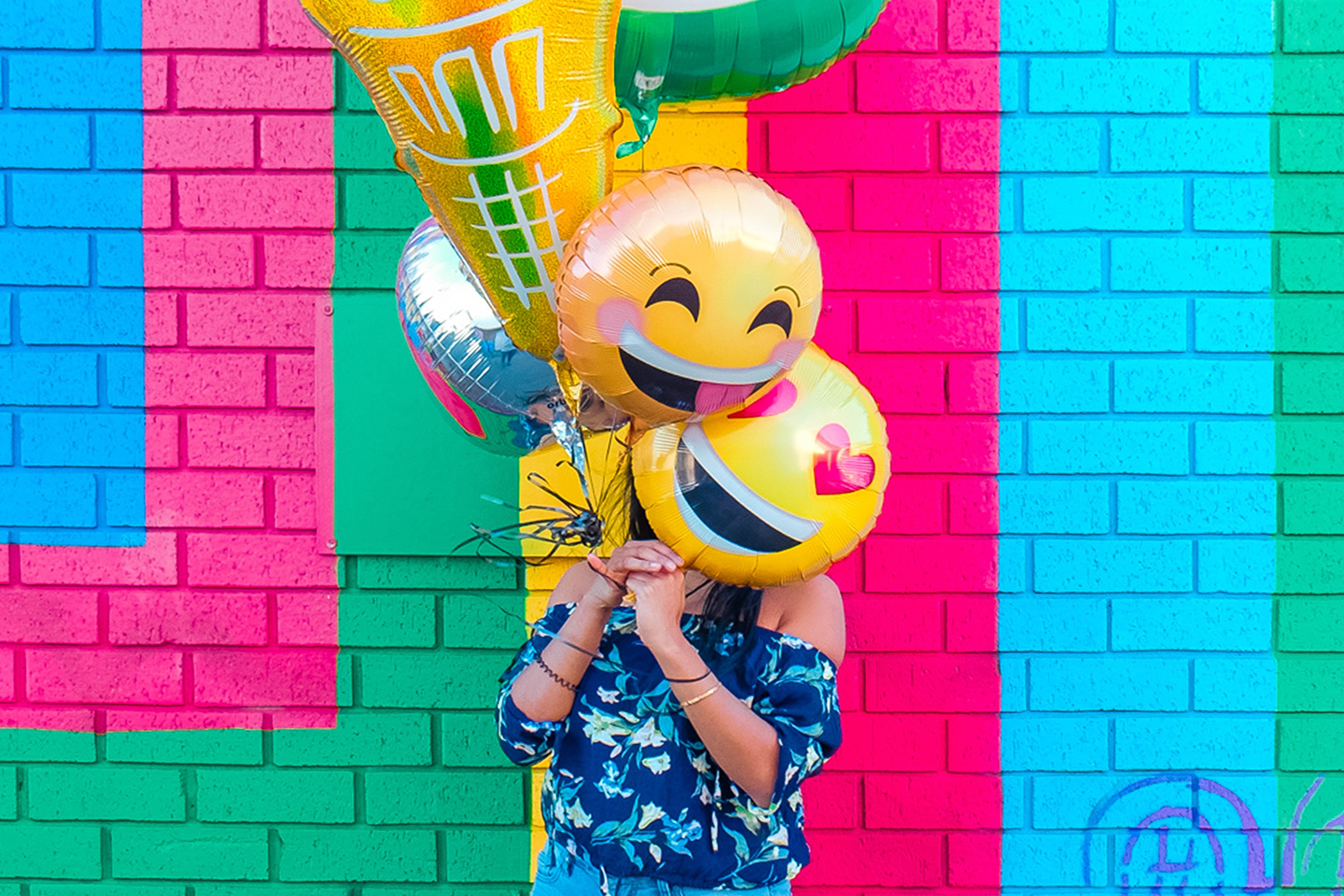 Woman holding emoji balloons in front of a colourful wall