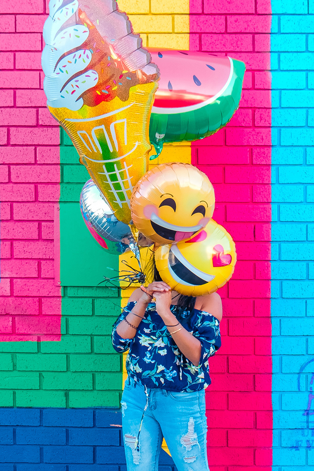Woman holding emoji balloons in front of a colourful wall